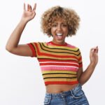 excited and happy girl having fun at party yelling from joy and thrill as dancing, enjoying cool music raising hands smiling broadly feeling awesome over white background in stylish 90s outfit
